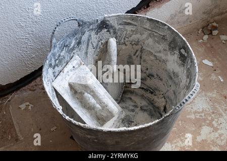 Trowels and other tools sit in a bucket on a construction site, covered in dust and debris during a home renovation project Stock Photo