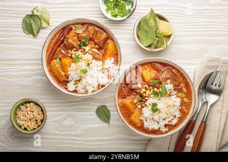 Two bowls of delicious massaman curry with beef, potatoes, rice, and peanuts, garnished with parsley on white wooden background, Thai cuisine Stock Photo