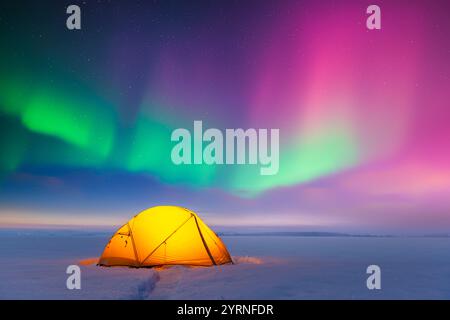 Yellow tent lighted from the inside against the backdrop of incredible starry sky with purple and green Aurora borealis. Amazing night landscape. Northern lights in winter field Stock Photo