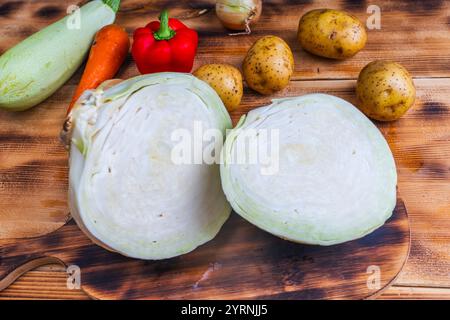 White cabbage cut into two halves or pieces on a wooden table with potatoes, red peppers, carrots and zucchini. High quality photo Stock Photo