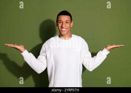 Young man in a white sweater poses smiling with arms extended against a khaki background Stock Photo