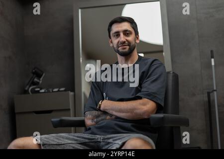 Stylish man in black T-shirt sits in chair in barbershop Stock Photo