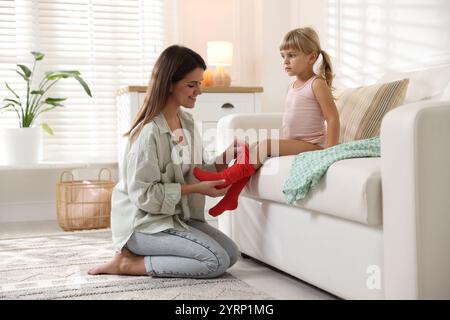 Mother helping her daughter to put tights on at home Stock Photo