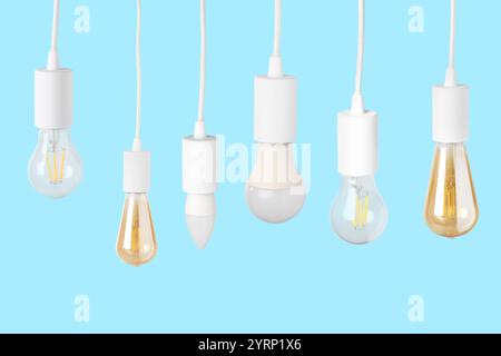 Different light bulbs hanging on light blue background Stock Photo