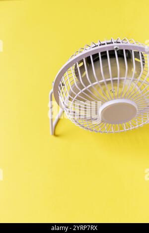 Creative mini fan stands and blows on a yellow background. Heat and air conditioning Stock Photo