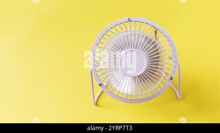 metal fan stands on a yellow background and blows. Heat and airflow, creative Stock Photo