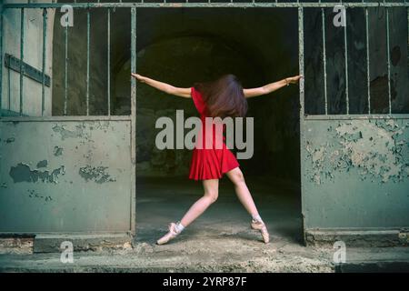 A  ballerina in  red dress performs a dramatic pose in an industrial setting with peeling paint, blending elegance with urban decay for a cinematic ef Stock Photo