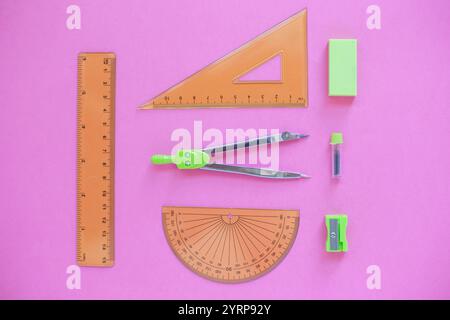 Green Set of geometry tools with compass, rulers, sharpener and eraser lies on a pink background, top view Stock Photo