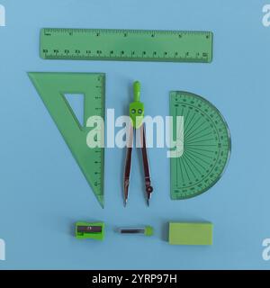 green set of geometry tools with compass, rulers, eraser and sharpener lie on a blue background, top view. Mathematics and study Stock Photo