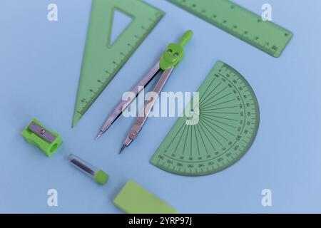 set of green geometry tools: rulers, compasses, eraser and sharpener lie on a blue background. Mathematics and lesson at school Stock Photo