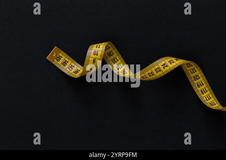 Yellow measuring tape centimeter lies on a black background. Nutrition and diet, concept Stock Photo