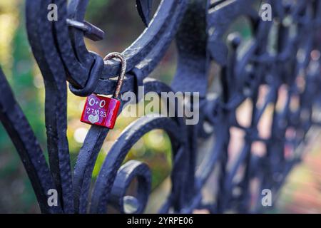 The red lock of the newlyweds with the written date hangs on the cast-iron fence. Stock Photo
