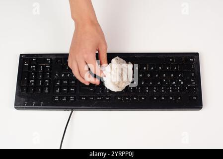 Cleaning computer keyboard in office with a wet wipe rag, dusty and dirty electronic, housework Stock Photo