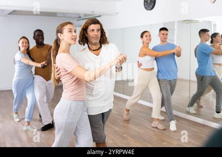 Smiling dancing people practicing movements while dancing in pairs in dance school for adults Stock Photo