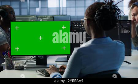 IT technician looking at green screen PC, working in data center, ensuring optimal performance. Employees monitoring energy consumption across server rigs using chroma key monitor, camera A Stock Photo