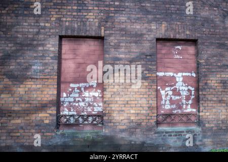 Weathered brick wall with two boarded up windows and peeling paint Stock Photo