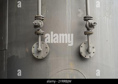 Close-up of industrial pipes and valves attached to a large metal tank, showcasing the intricate network of a processing facility Stock Photo