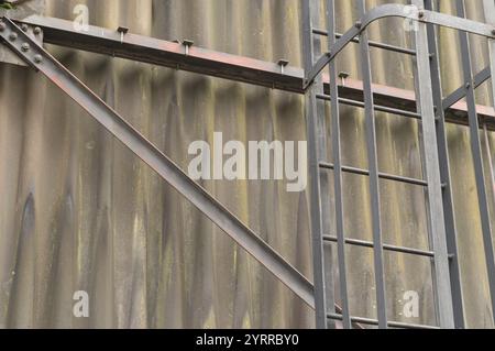 Close-up of a metal ladder and support beam attached to a corrugated metal wall, showing signs of weathering and rust Stock Photo