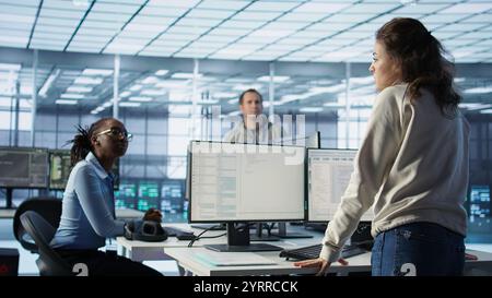 Manager overseeing server room holding impromptu meeting with employees. Supervisor in server hub, asking for attention to offer feedback to workers after doing inspection, camera B Stock Photo