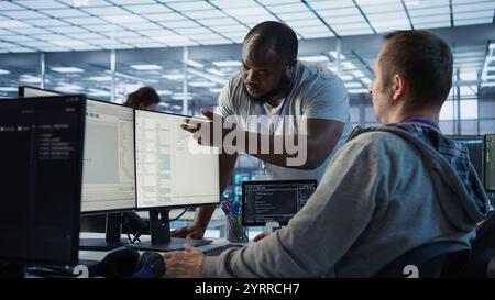 Engineer having fun with colleague at work in data center establishment, making jokes. Team of technicians making each other laugh, bonding in server room, doing fist bump gesture , camera B Stock Photo