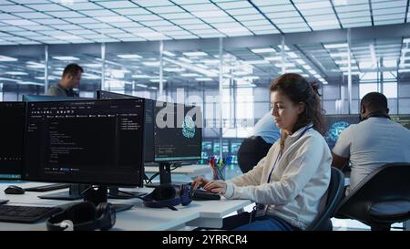 Upbeat computer scientist working in high tech server hub capable of processing vast amounts of data. Smiling woman at PC typing on keyboard, updating servers controlling network resources, camera B Stock Photo