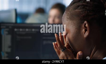 Tired software developer having eye strain while working on high tech data center computer. Overworked african american woman removing glasses to relax eyes in server room, camera A close up Stock Photo