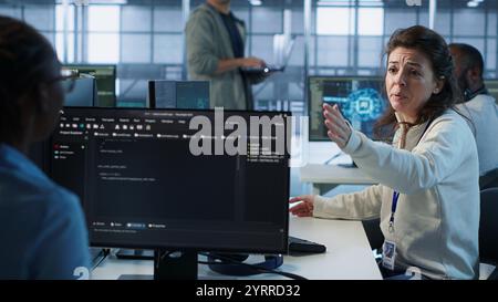 Angry woman getting computer crash while trying to fix error in high tech data center. Furious employee in server farm struggling to repair bugs in mainframes, arguing with colleagues, camera A Stock Photo