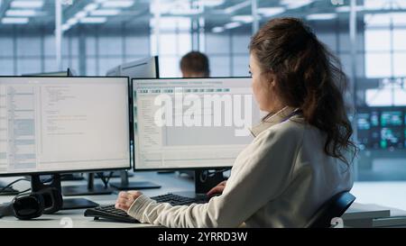 Smiling manager in server hub using computer to find firewall misconfigurations affecting rackmounts performance. Upbeat supervisor checking systems bottlenecks affecting data transfer rates, camera A Stock Photo