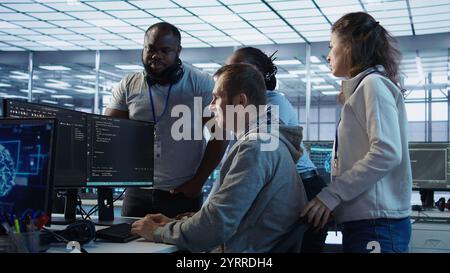 Technician doing brainstorming with colleagues to fix error in code affecting server room AI workloads. Team of artificial intelligence engineers repairing data center systems together, camera B Stock Photo