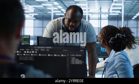 Manager doing team meeting with engineers, delegating tasks in high tech data center office. Supervisor doing brainstorming with IT experts how to while monitor AI supercomputers, camera A Stock Photo