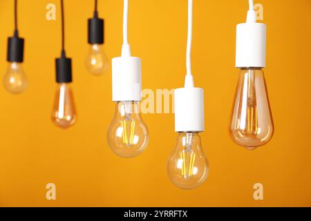 Light bulbs hanging on cords against orange background Stock Photo