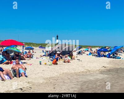 Robert Moses, New York, USA - 15 June 2024: Beachgoers lounge under umbrellas, enjoying the sun and the sea breeze by the lighthouse on a warm day. Stock Photo