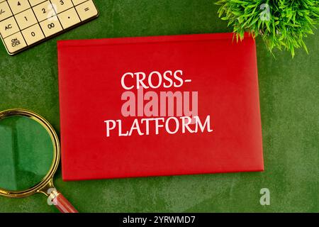 Context Marketing concept. Text CROSS-PLATFORM on the cover of a red notebook on a green saturated background. Stock Photo