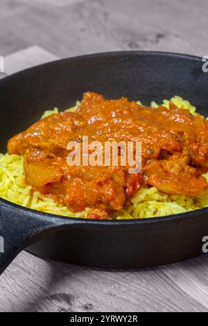 Chicken balti Indian hot spicy curry meal with pilau rice in a cast iron pan. On a wood board Stock Photo