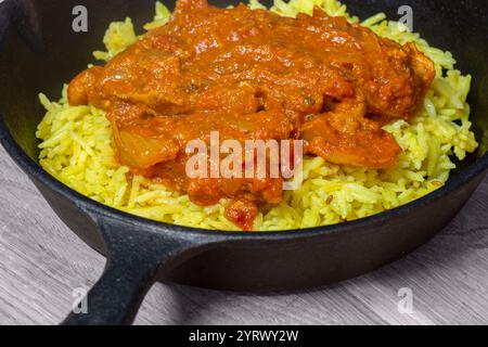 Chicken balti Indian hot spicy curry meal with pilau rice in a cast iron pan. On a wood board Stock Photo