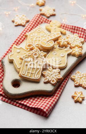 Delicious homemade christmas cookies shaped as snowflakes, gingerbread man, reindeer and houses lying on white cutting board on red checkered tableclo Stock Photo