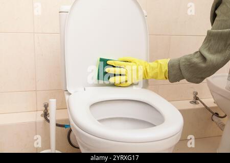 Home Cleaning in protective Yellow gloves, green sponge. Cleans Toilet with Household Chemicals. Toilet cleaning, Disinfection and Hygiene Eco Concept Stock Photo