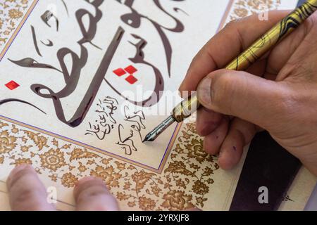 A calligrapher writing a name using a reed pen and ink at the Algiers International Book Fair (SILA), Algeria. Stock Photo