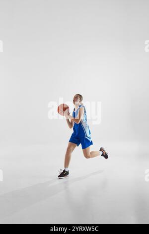 Scoring a goal. Full-length dynamic image of young teen girl in blue uniform in motion, training, playing against white studio background Stock Photo