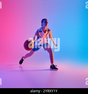 Dynamic image of young teen girl, basketball player in motion with ball, training, playing against gradient pink blue background in neon light Stock Photo