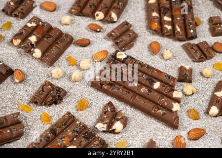 Broken chocolate pieces with nuts and raisins on a stone background Stock Photo