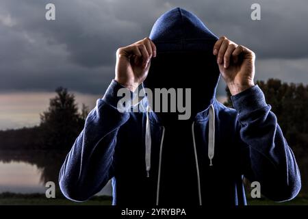Mysterious man covering face with hood in dramatic landscape Stock Photo