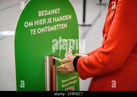 Person using a hand sanitizer station with a Dutch sign promoting hygiene and safety measures during the COVID-19 pandemic. Stock Photo