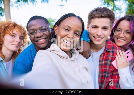 Diverse group of friends waving and smiling outdoors in a cheerful selfie Stock Photo