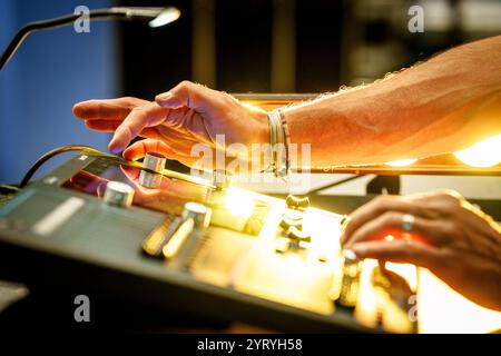 Close-up of a technician’s hands operating a sound mixing console, illuminated by stage lighting, emphasizing audio production at a live event. Stock Photo