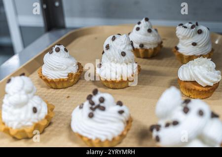 Shortcrust pastry tartlets with fluffy white cream or cream, decorated with chocolate on a tray on the production table, in a pastry shop or workshop. Stock Photo