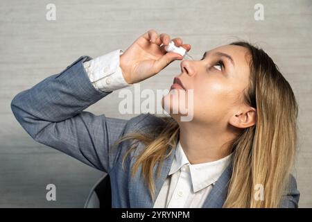 Female entrepreneur freelancer working on laptop and holding medicinal eye drops to relief eye strain and dryness, due to overwork on laptop. Digital Stock Photo