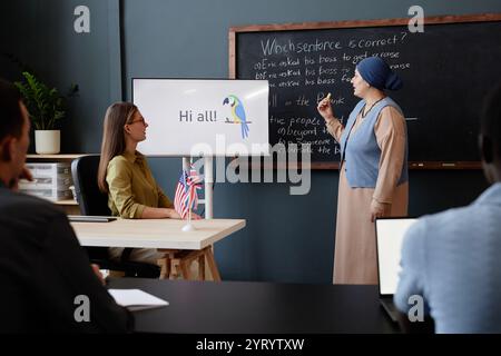 Side view of young Muslim woman explaining multiple choice task answering at chalkboard while studying English grammar in class at language school Stock Photo