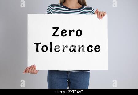 Woman holding poster with words Zero Tolerance on light grey background, closeup Stock Photo