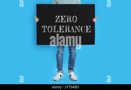 Man holding poster with words Zero Tolerance on blue background, closeup Stock Photo